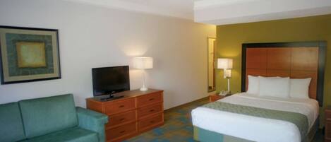 A hotel room with a bed, a television on a wooden dresser, a green sofa, and a patterned carpet.