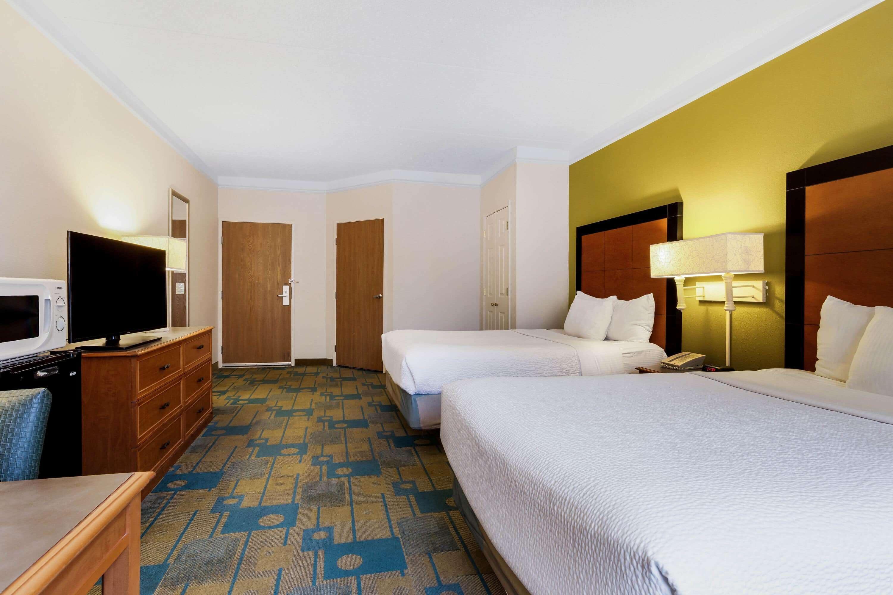 Habitación de hotel con dos camas, televisión, escritorio y puerta al baño.