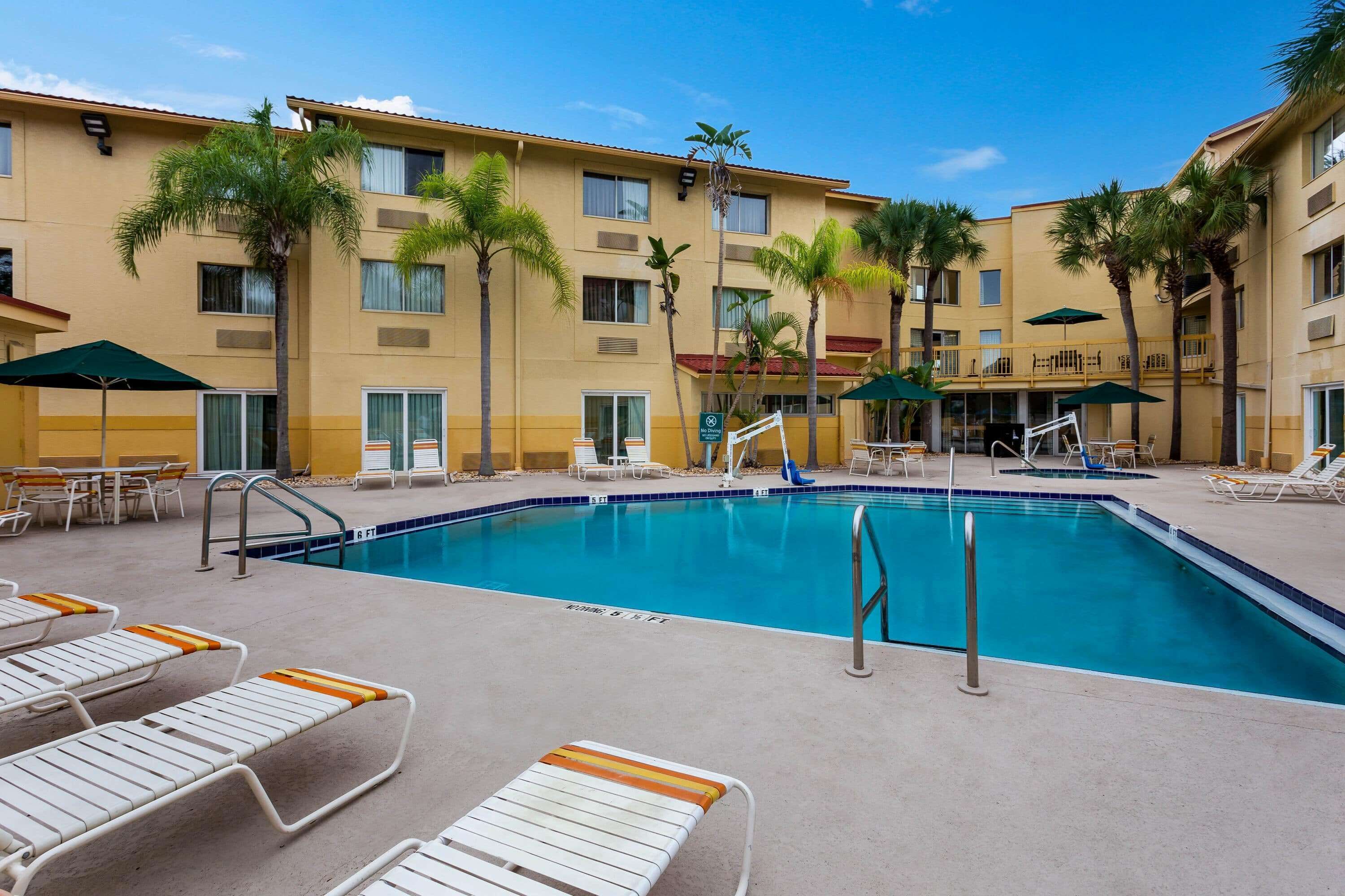A hotel pool area with lounge chairs, palm trees, and a clear blue pool.