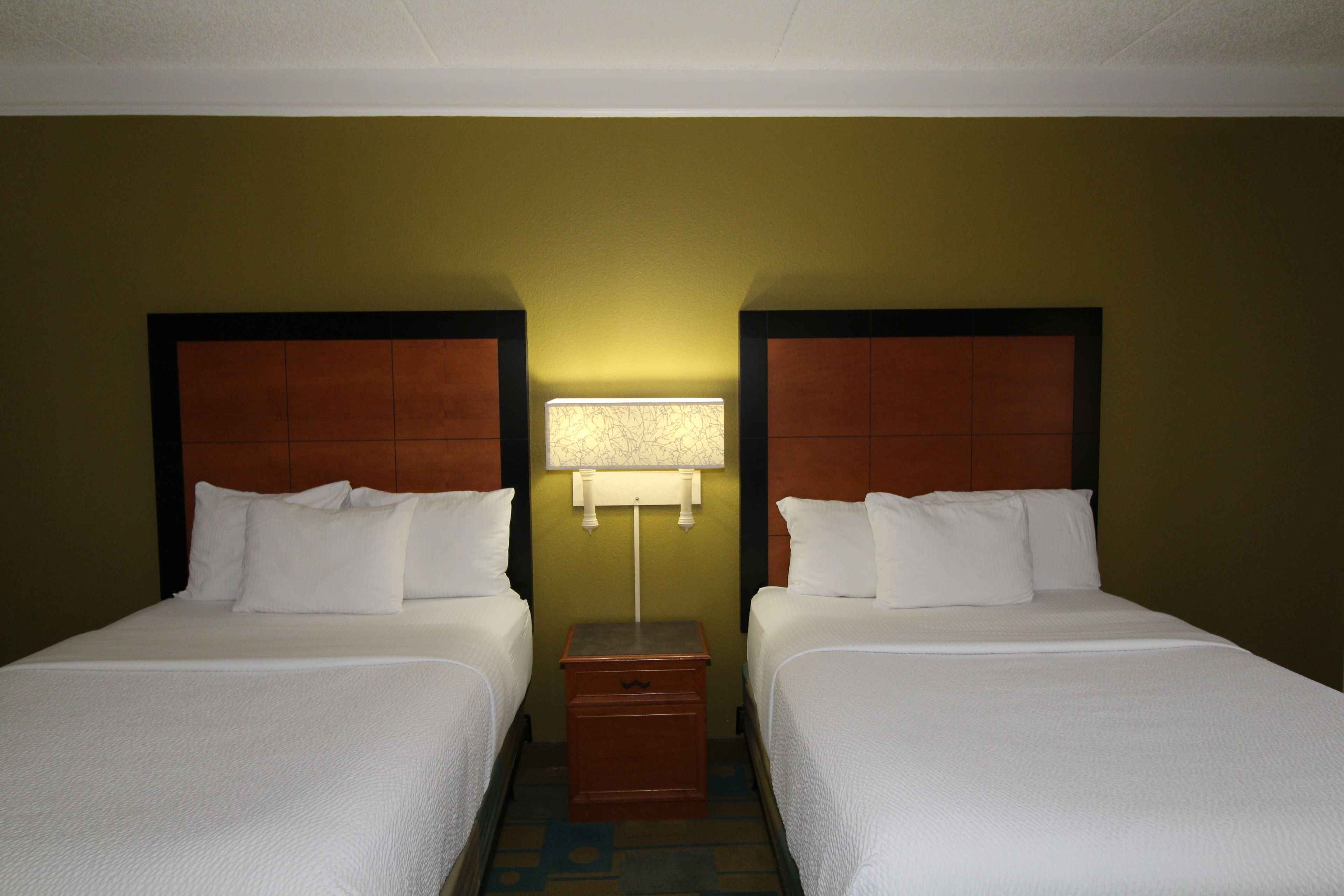 A hotel room with two beds, a nightstand, and a wall-mounted lamp.