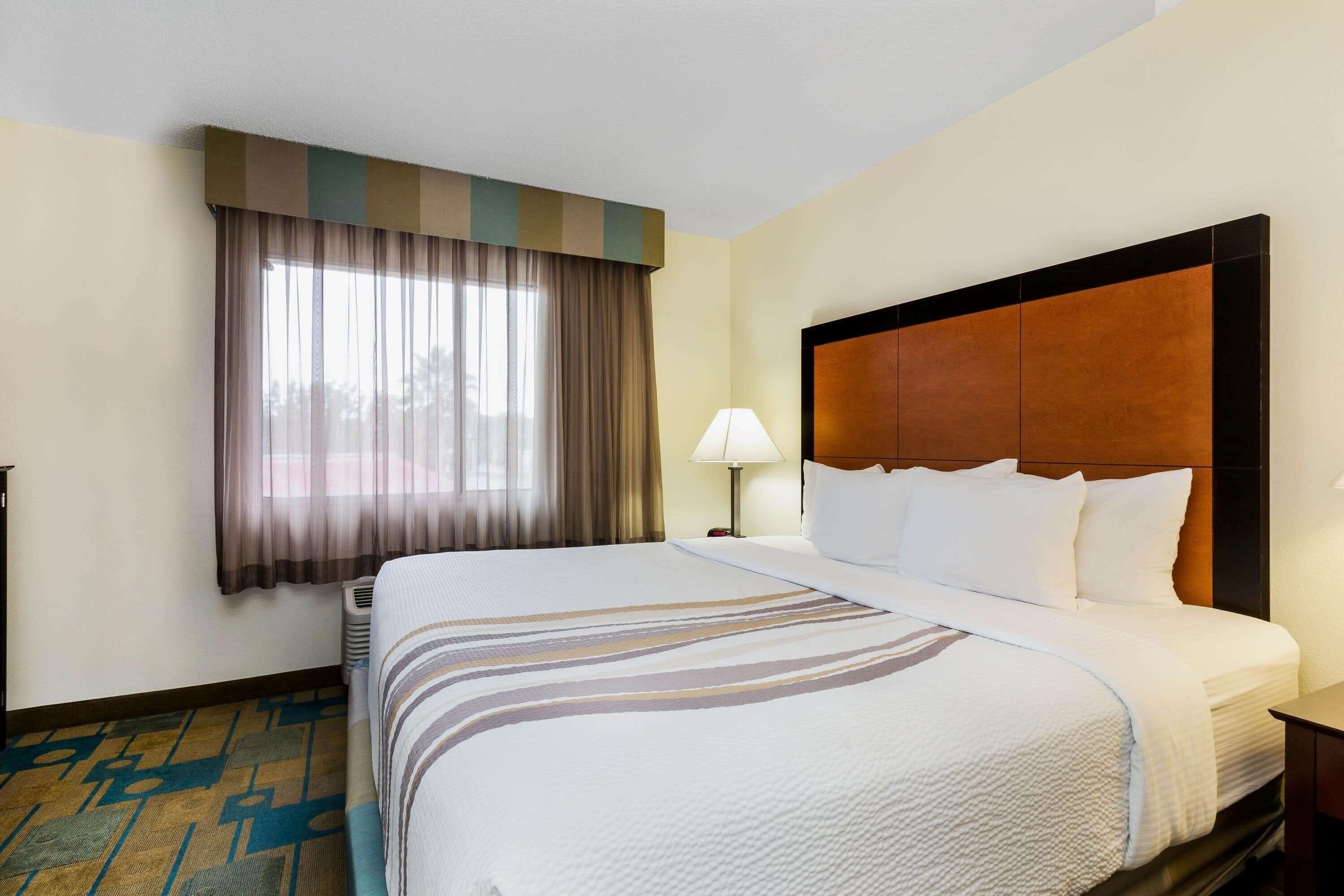 A hotel room with a large bed, a nightstand, a lamp, and a window with curtains.