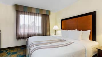 A hotel room with a large bed, a nightstand, a lamp, and a window with curtains.