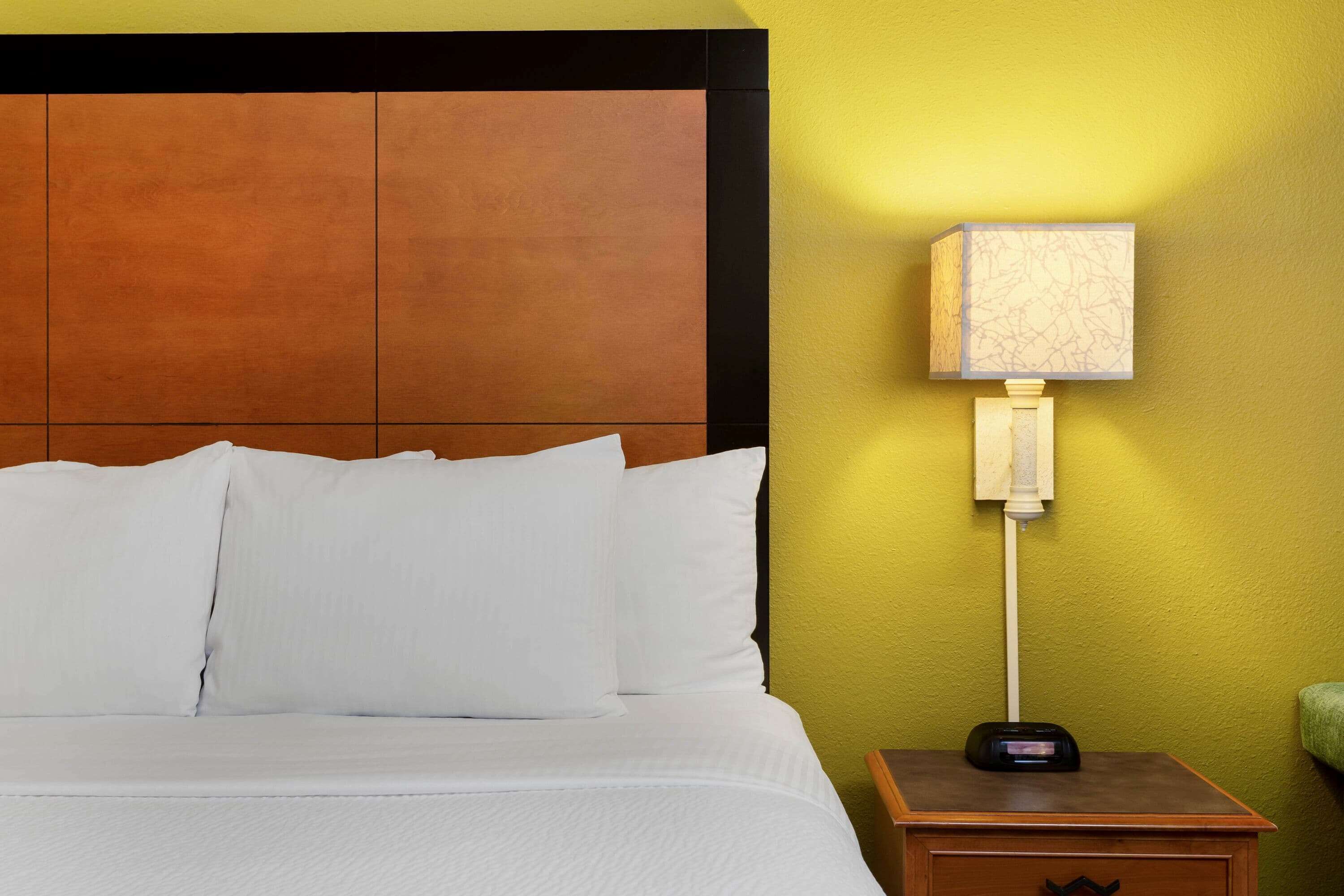 Une chambre d’hôtel avec un lit, du linge de lit blanc, une table de chevet avec une lampe et une tête de lit en bois.