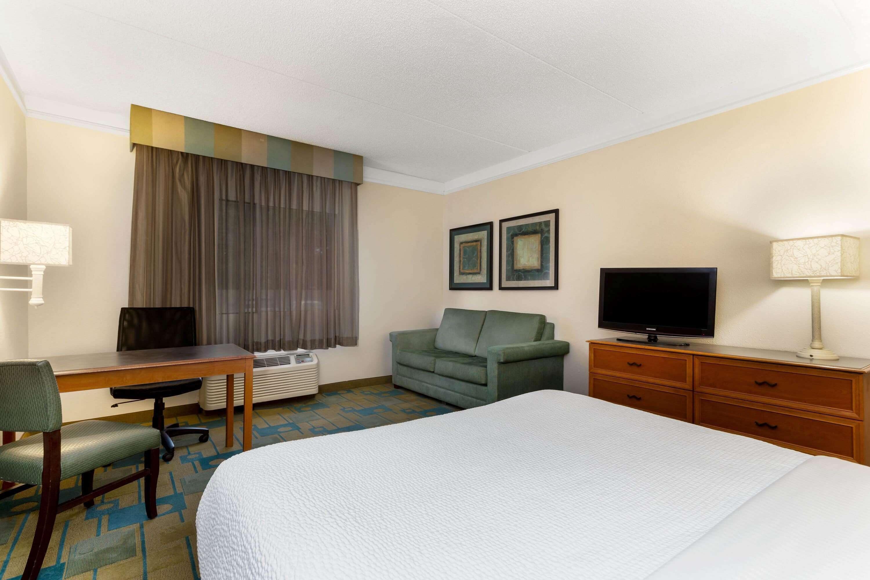 Une chambre d’hôtel équipée d’un lit, d’un bureau, d’une chaise, d’un canapé, d’une télévision et d’une commode.