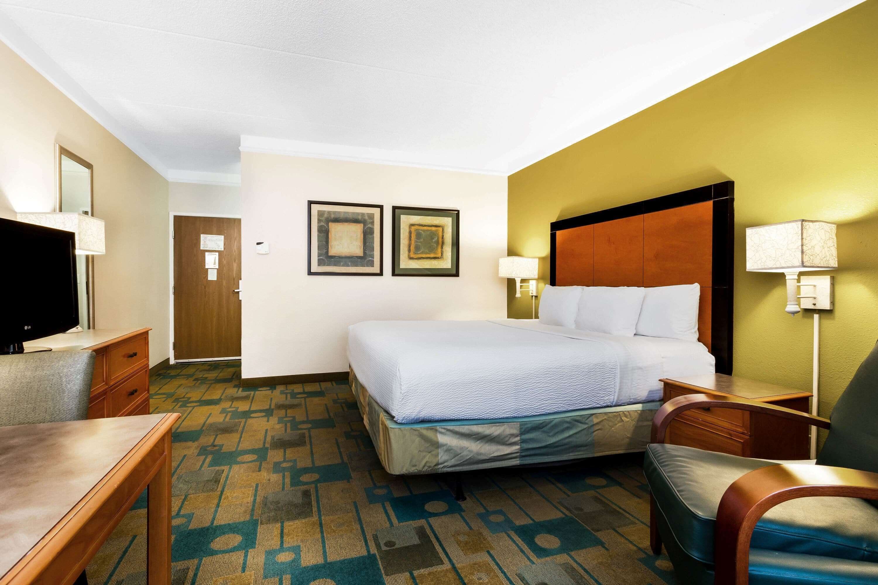 A hotel room with a bed, a desk, a chair, a television, and two framed pictures on the wall.