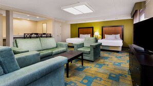 A hotel room with a sofa, armchairs, a small table, a bed with two pillows, a TV, and a bathroom with a mirror and sink. - La Quinta Inn & Suites by Wyndham St. Pete-Clearwater Airpt (Clearwater)