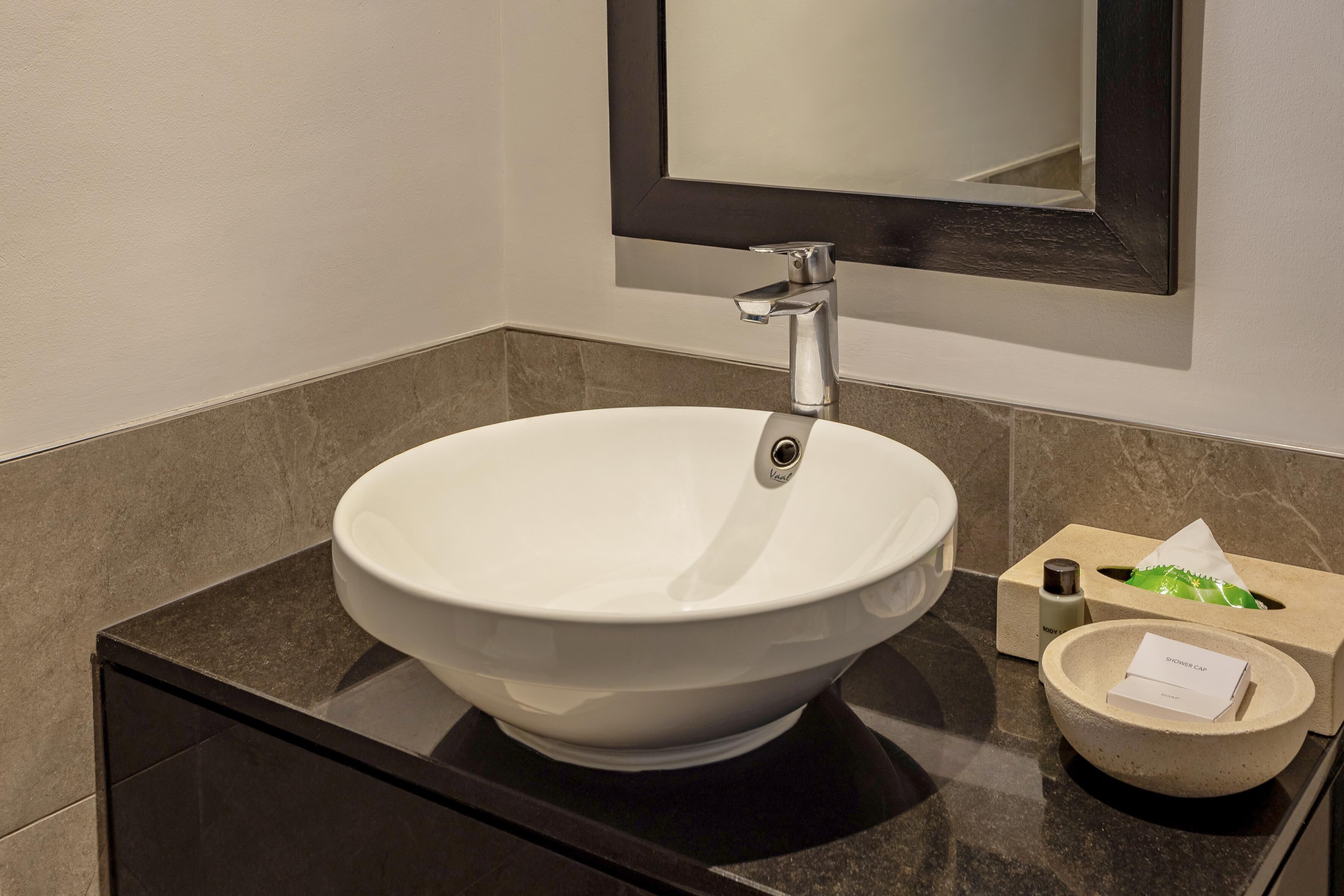 A modern bathroom with a white vessel sink, a mirror above it, and a small round basin with a shower cap.