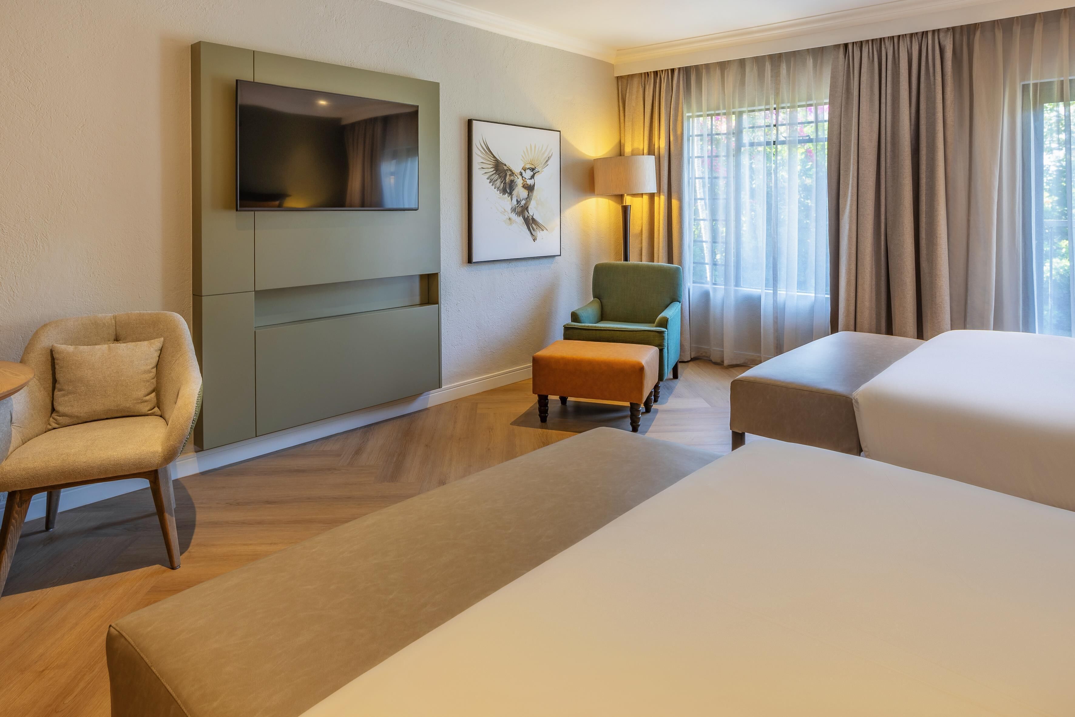 A hotel room with a bed, a chair, a sofa, a TV, and a lamp.
