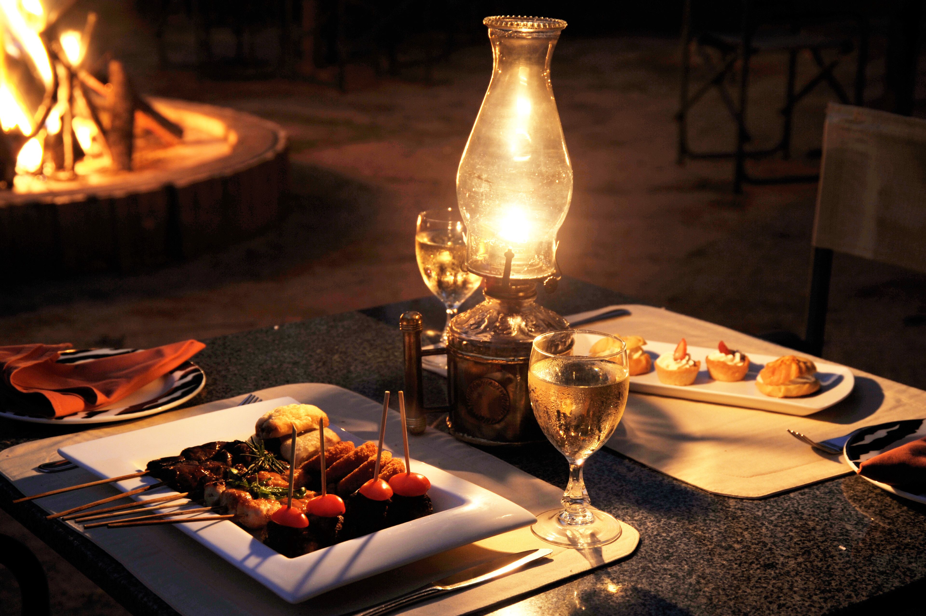 A candlelit table with a bottle, a glass, and a plate of food.