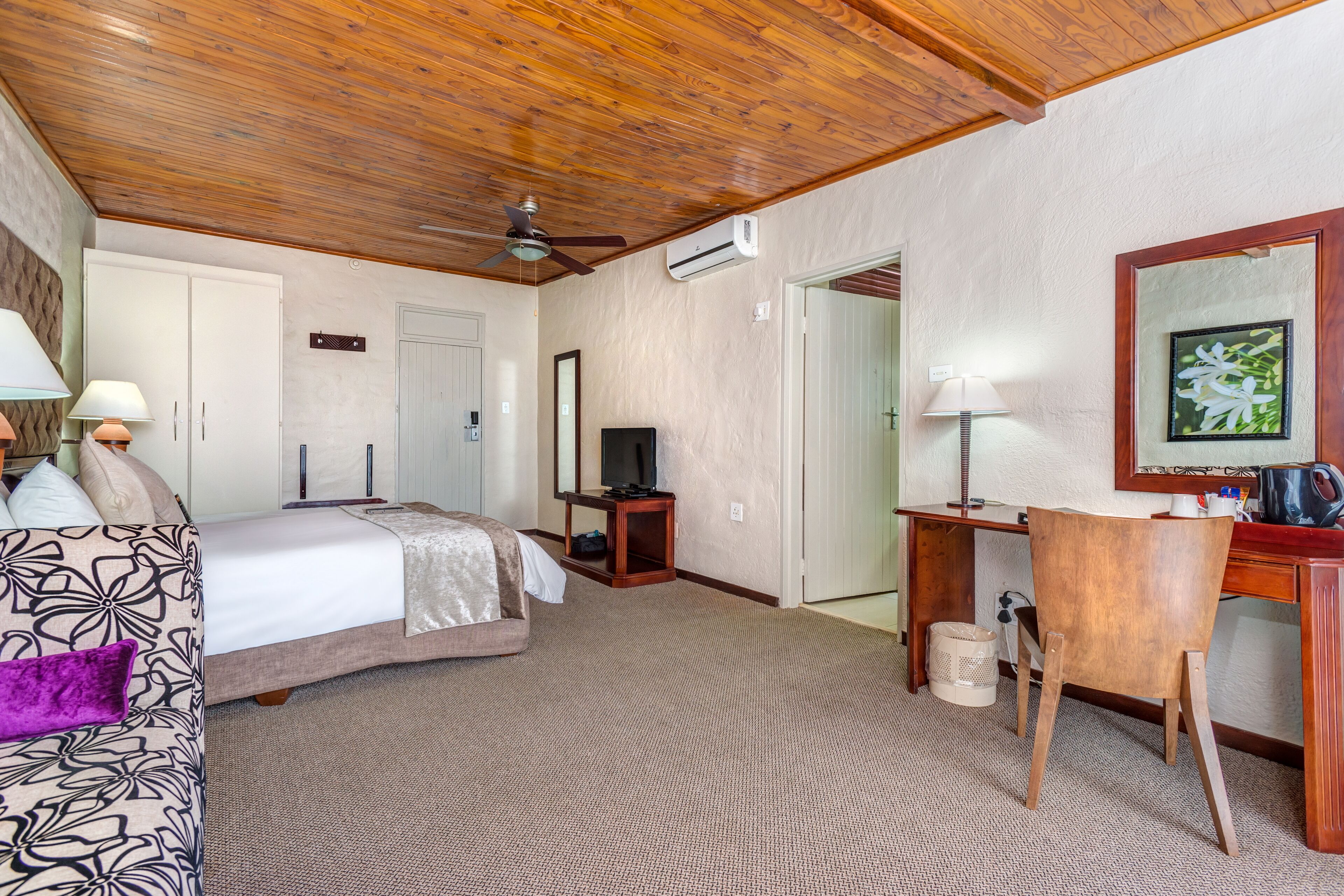 A hotel room with a bed, desk, chair, and ceiling fan.