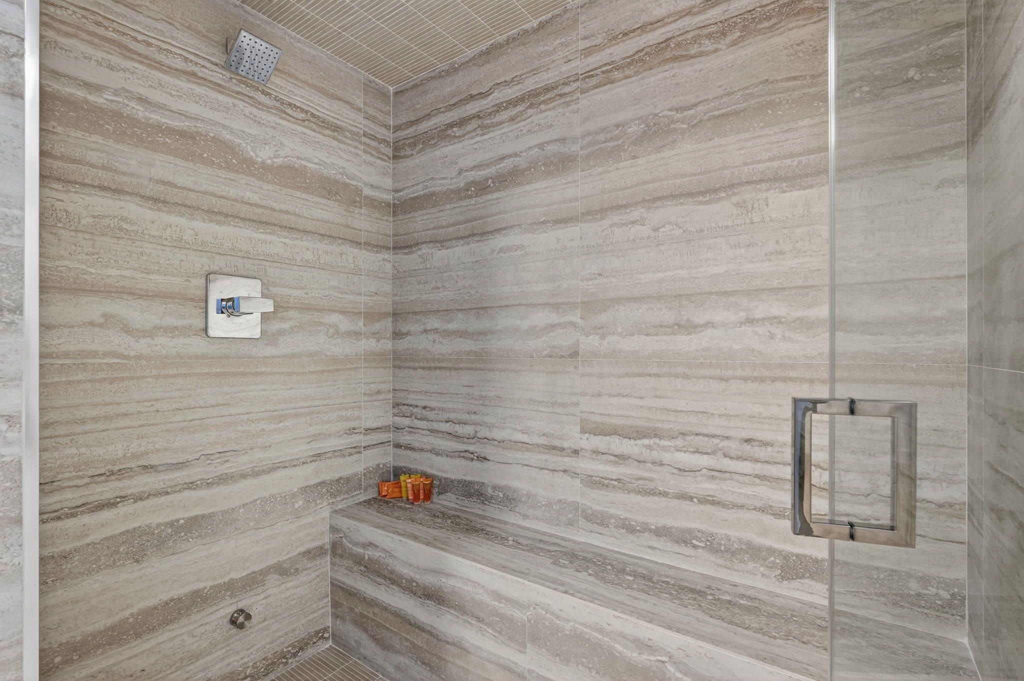 Una ducha con pared de mármol, un perchero y un cabezal de ducha.