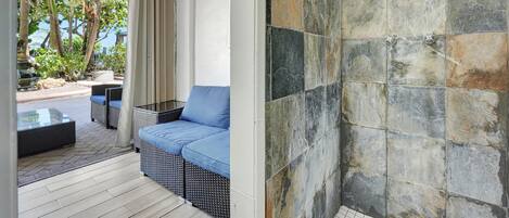 A room with a sofa and a glass table, a tiled shower wall, and a view of trees and a rock formation outside.