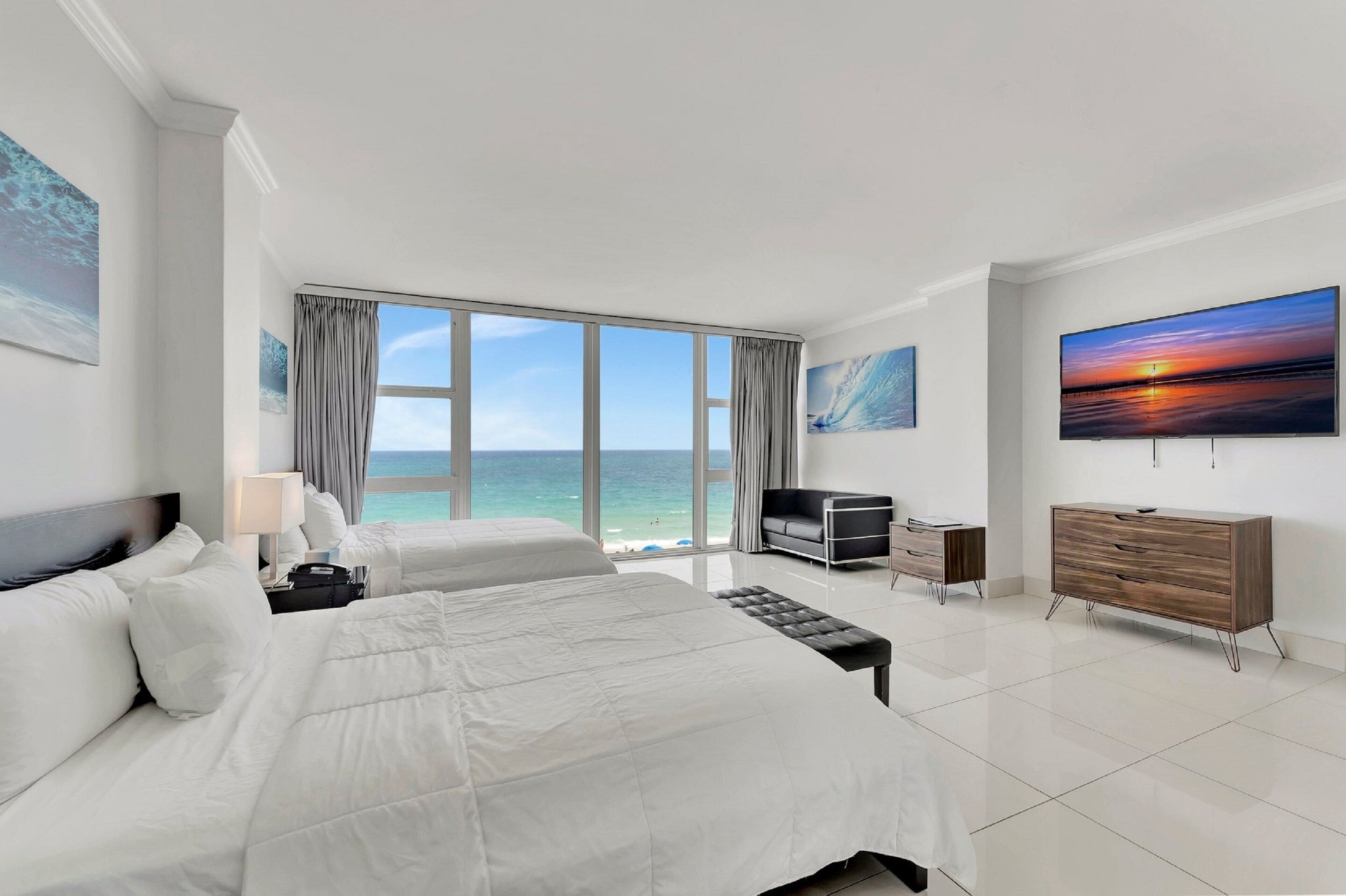 Ein Hotelzimmer mit einem großen Bett, einem Fernseher, einem Schminktisch und Blick aufs Meer.
