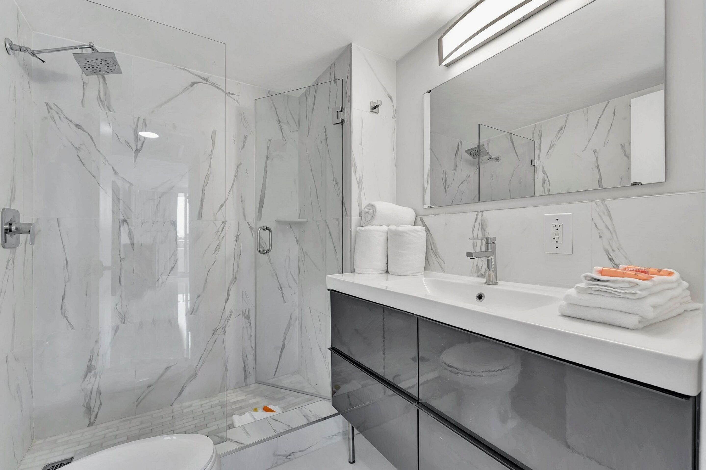 A modern bathroom with a glass-enclosed shower, a white sink with a mirror above, and a black cabinet below.