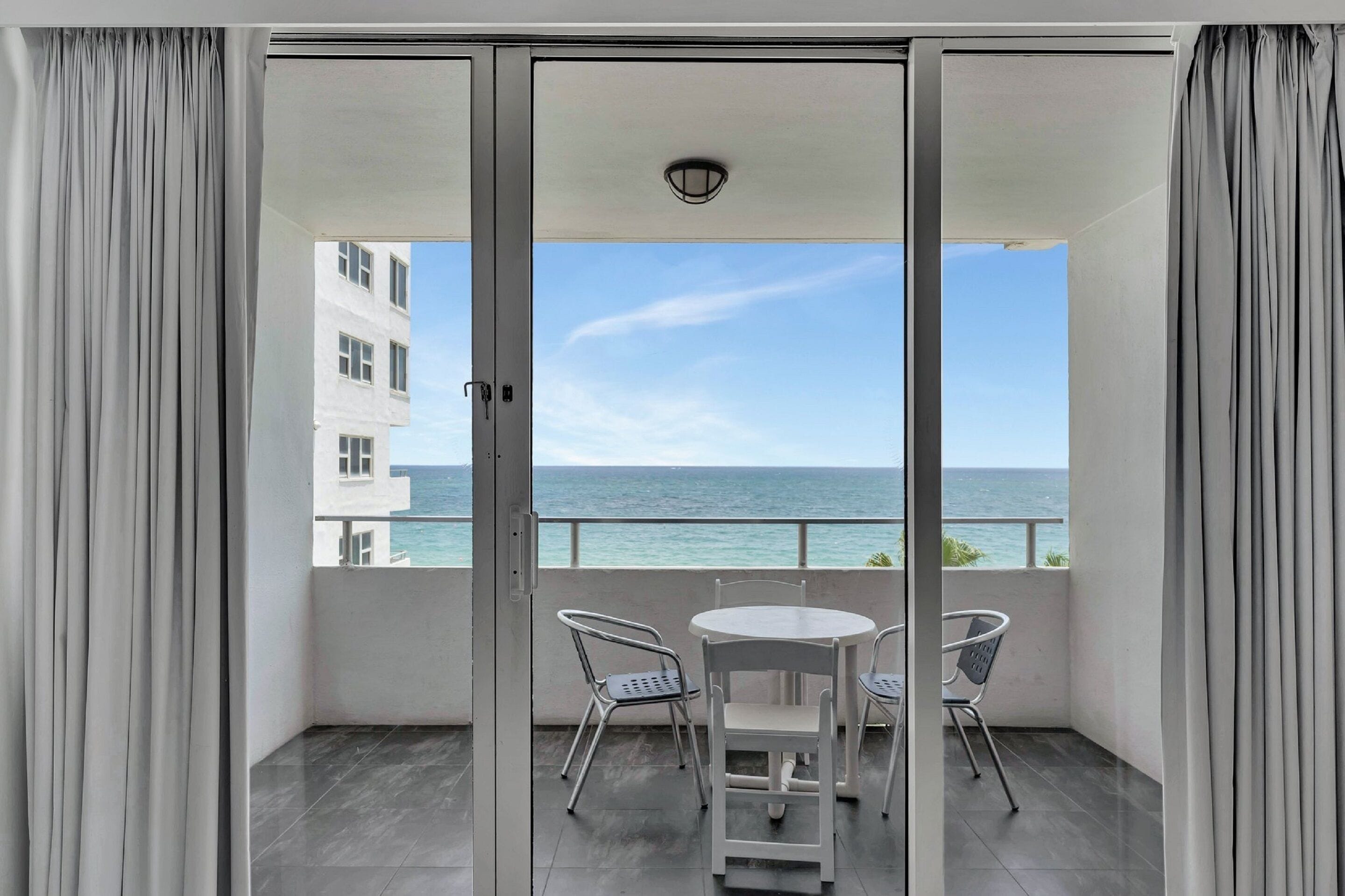 A balcony with a table and chairs, offering a view of the sea and a building across the water.