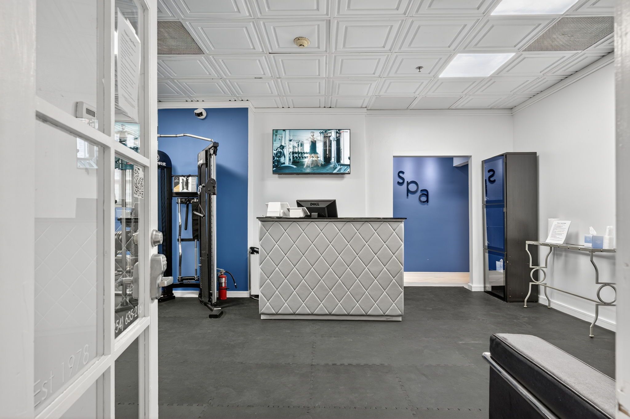 A reception area with a reception desk, a blue wall with 'spa' signage, a fire extinguisher, and a large window.