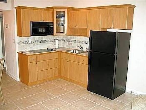 A compact kitchen with wooden cabinets, a black refrigerator, and a tiled backsplash. - Ocean Manor Beach Hotel (Fort Lauderdale)