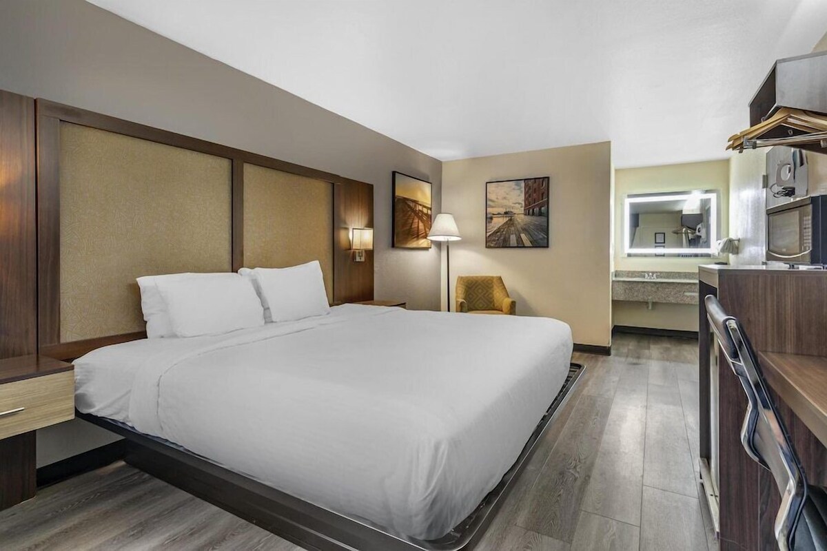 Une chambre d’hôtel comprenant un lit, une table de chevet, une lampe, une chaise et une kitchenette.