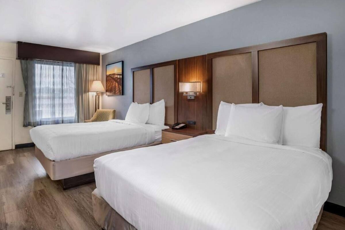 A hotel room with two beds, a desk, a lamp, and a window with curtains.