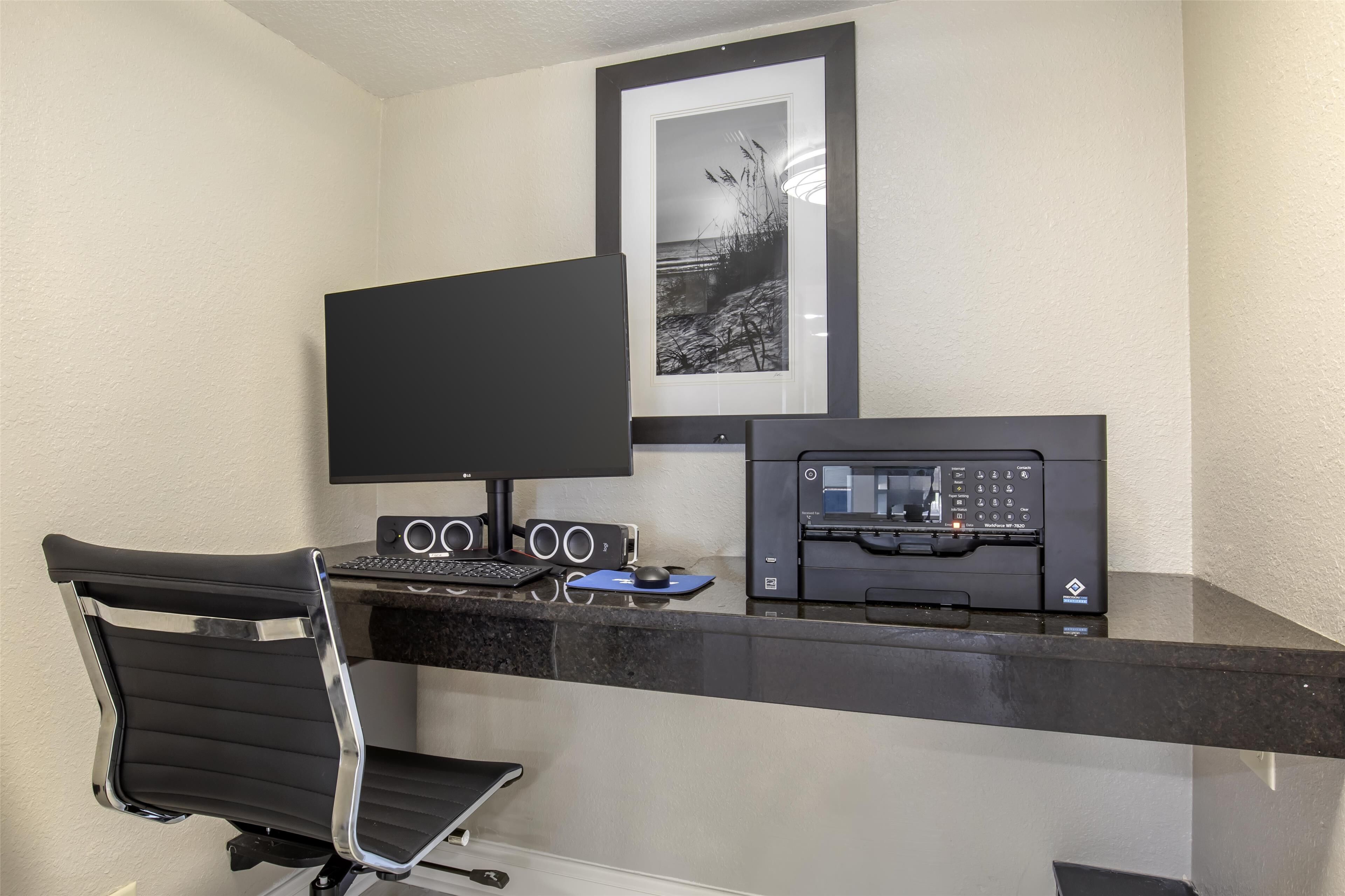 Un espacio de oficina moderno con un escritorio negro, una computadora, una impresora y un cuadro en la pared.