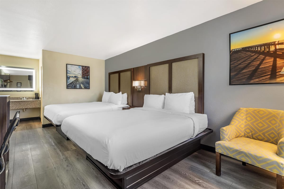 A hotel room with two beds, a desk with a lamp, a chair, and a painting on the wall.