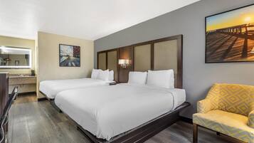 Habitación de hotel con dos camas, un escritorio con lámpara, una silla y un cuadro en la pared.