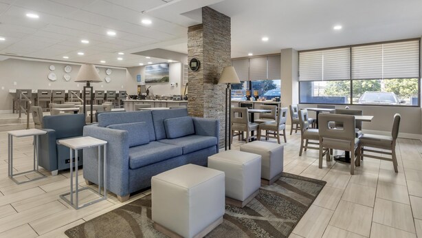 Un moderno vestíbulo de hotel con un sofá azul, otomanas blancas y una zona de comedor con mesas y sillas.