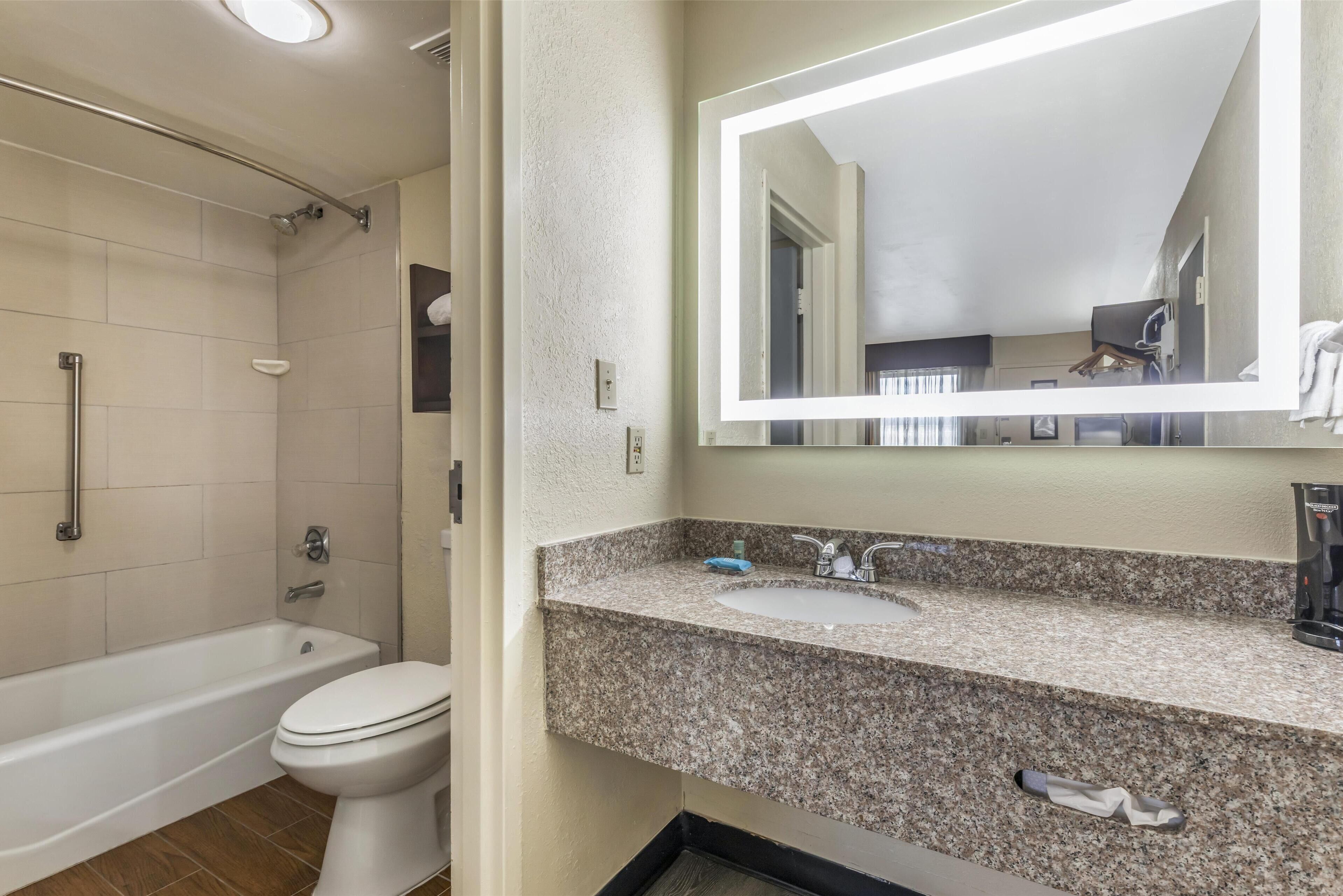 A bathroom with a bathtub, toilet, and granite countertop sink.