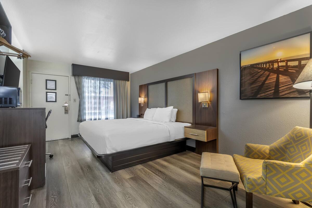 A hotel room with a large bed, a desk with a chair, a TV, and a painting on the wall.