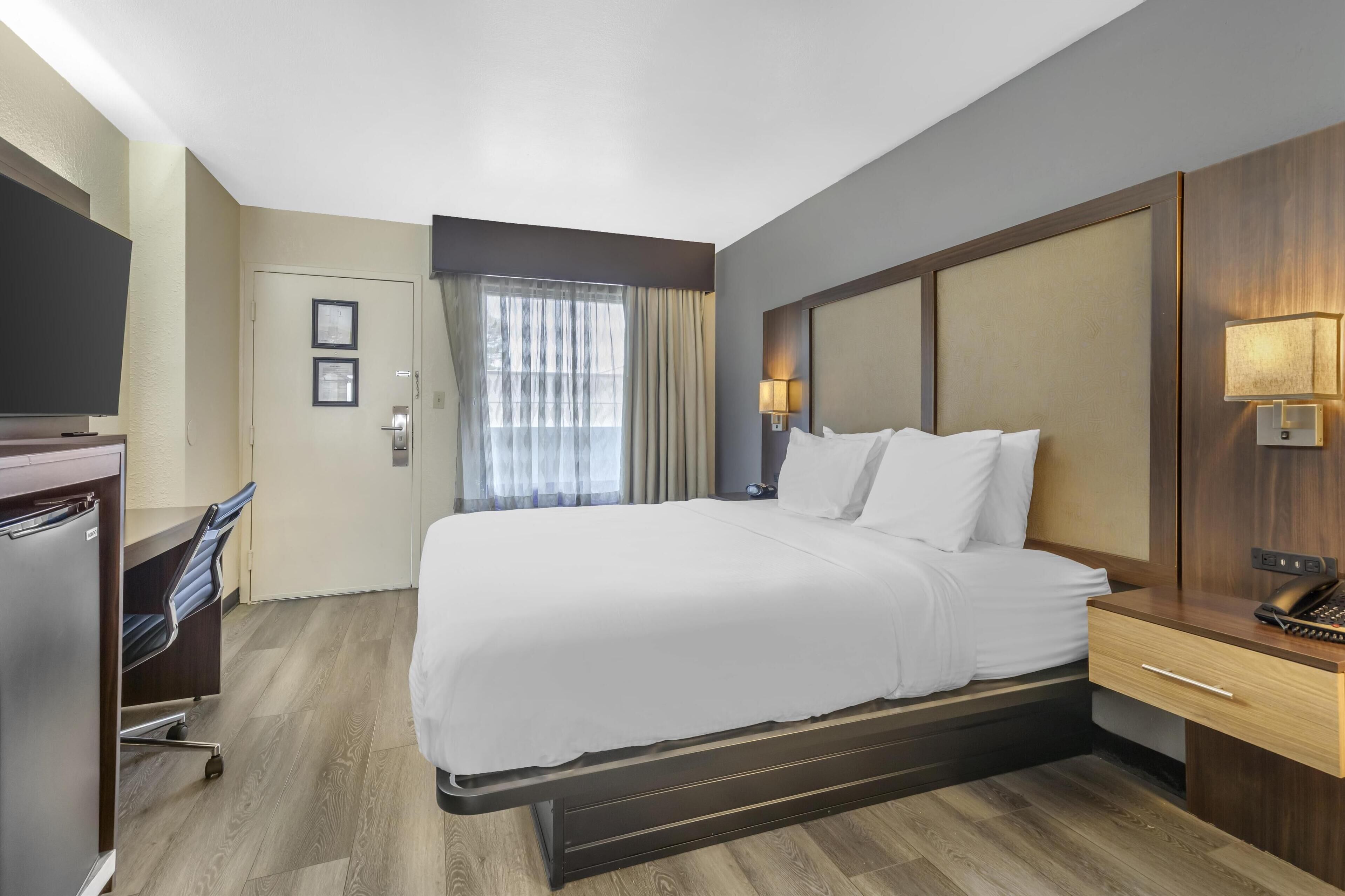 A hotel room with a large bed, a desk with a chair, a television, and a window with curtains.