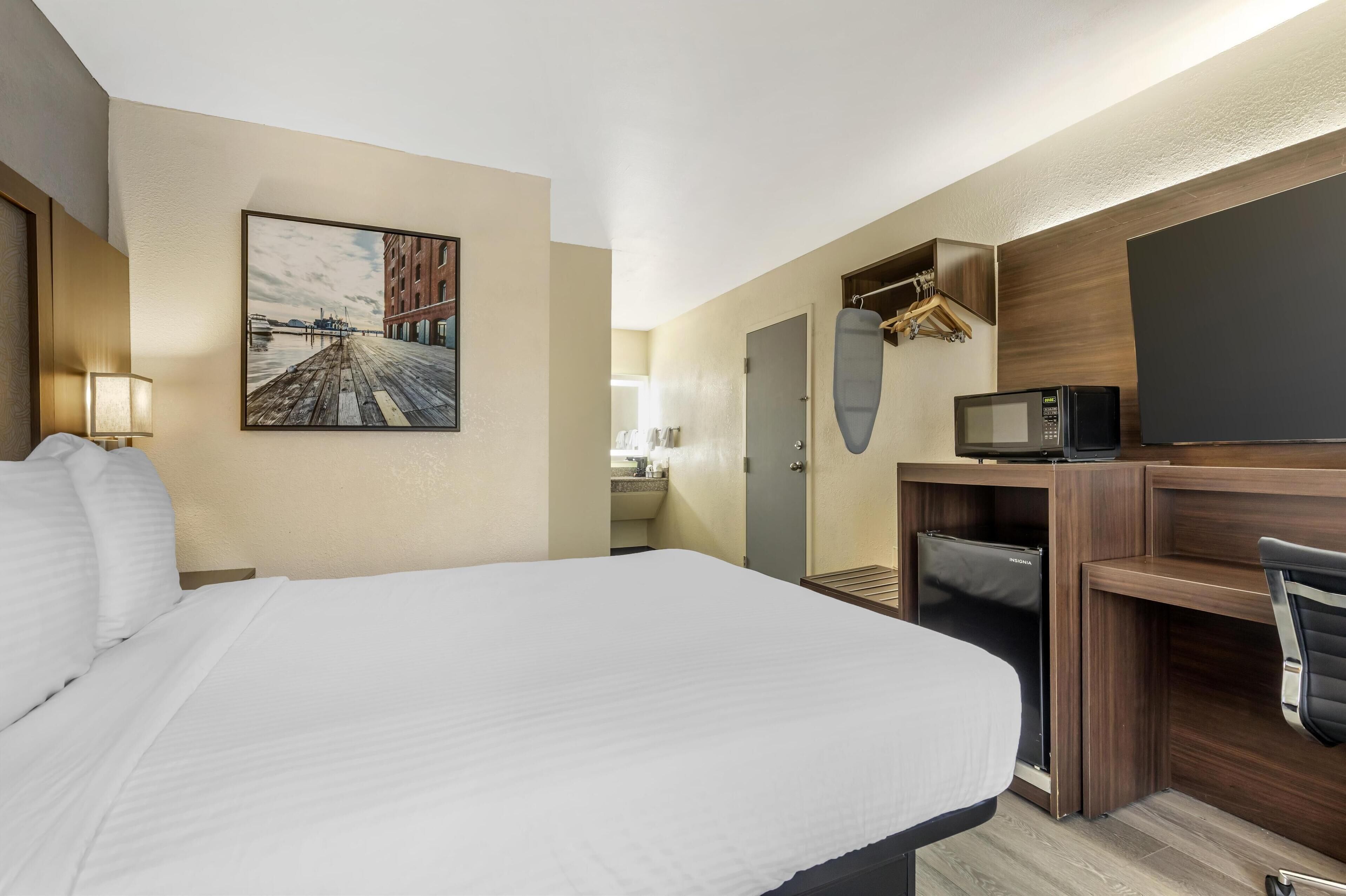 A hotel room with a large bed, a desk with a computer, a microwave, and a TV.