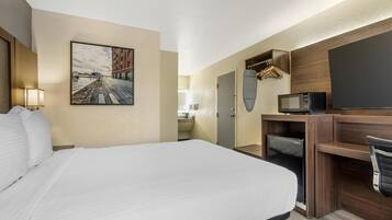 A hotel room with a large bed, a desk with a computer, a microwave, and a TV.