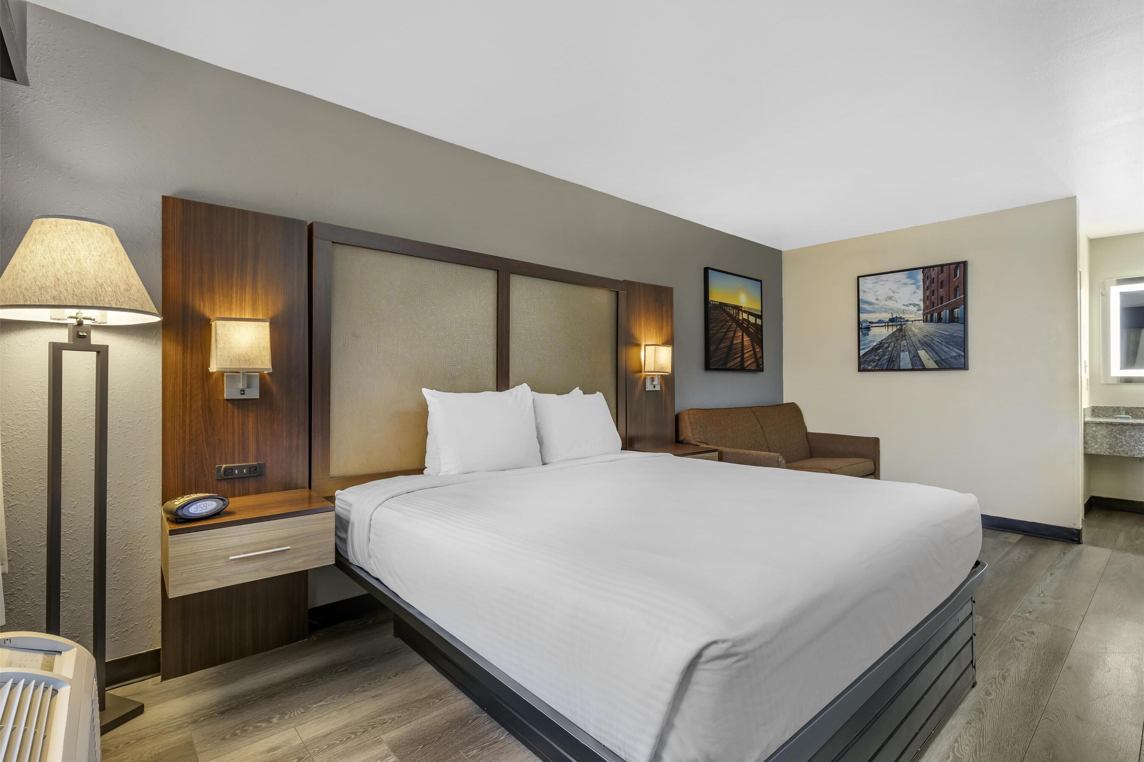 Een hotelkamer met een groot bed, nachtkastjes met lampen, een zithoekje en kunst aan de wanden.