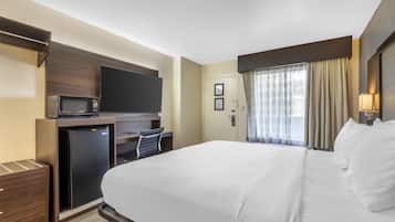 Habitación de hotel con cama, escritorio con televisor, refrigerador y ventana con cortinas.