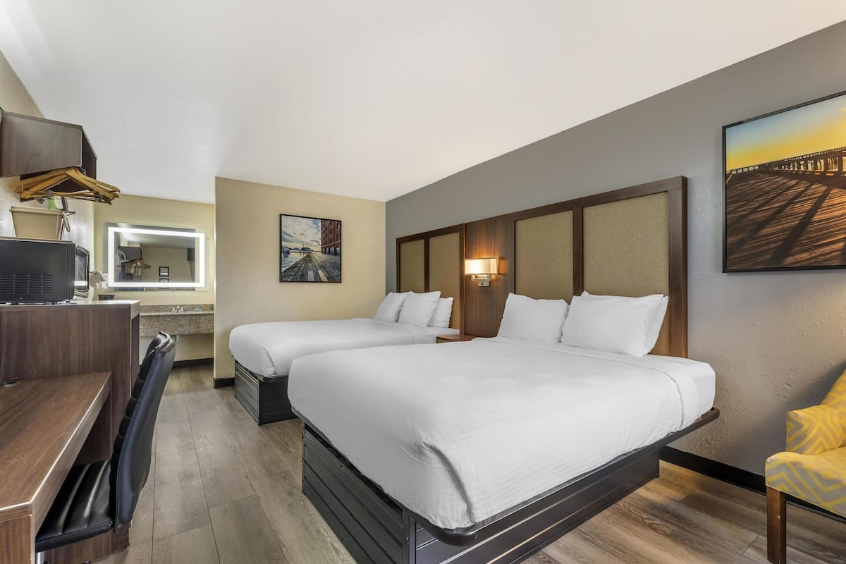 A hotel room with two beds, a desk, a chair, a TV, and a painting on the wall.
