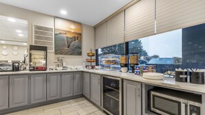 Una cocina moderna con armarios grises, microondas, cafetera y un amplio ventanal con vistas al estacionamiento.
