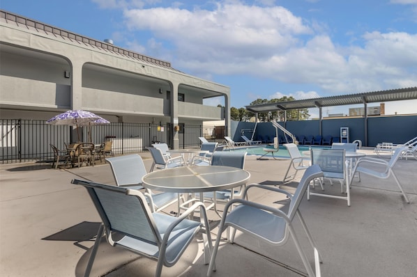 An outdoor seating area with lounge chairs and a table, a pool, and a building with a flat roof. - Best Western Salisbury Plaza (Salisbury)