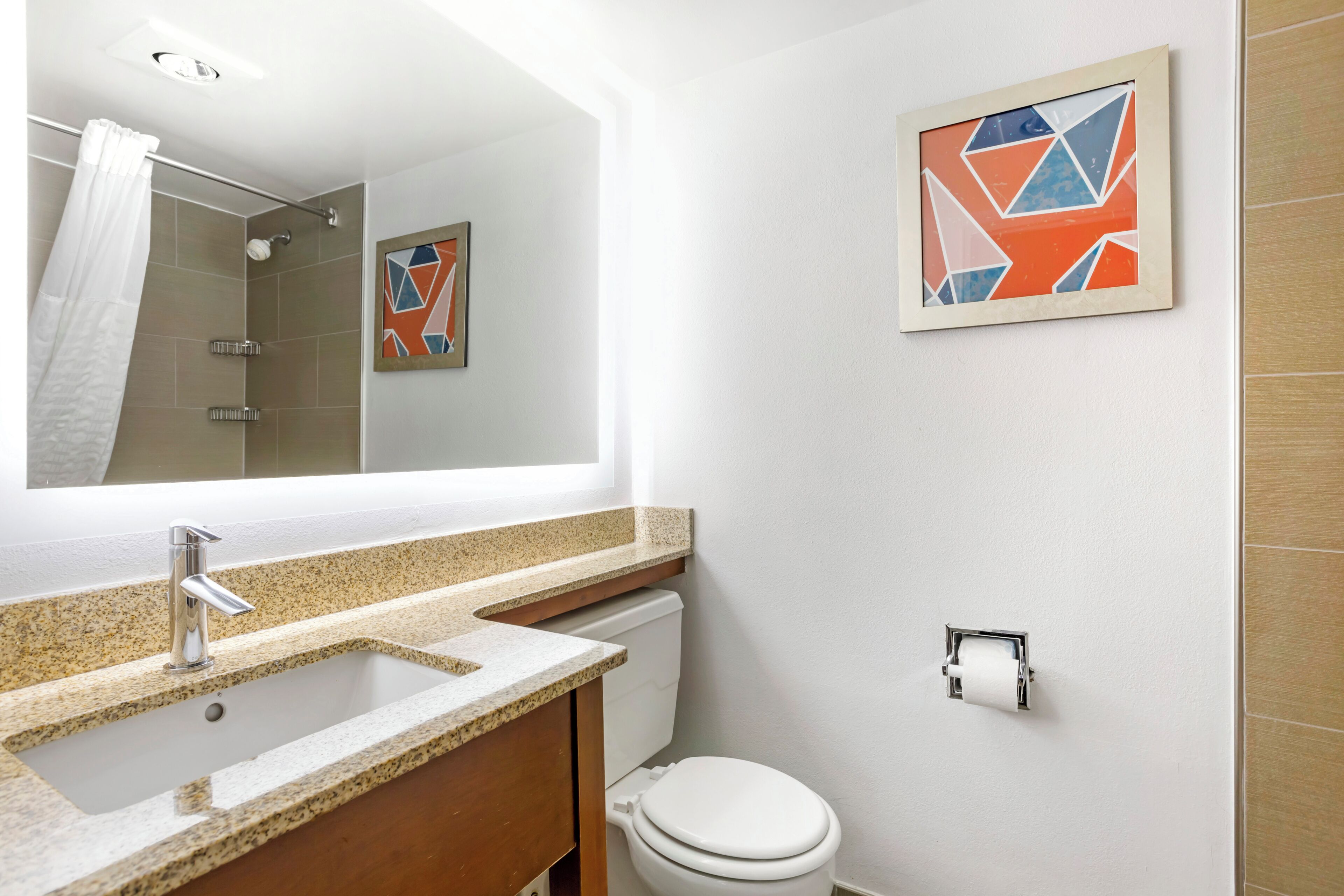 A bathroom with a sink, toilet, shower, and a framed abstract art piece on the wall.