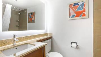 A bathroom with a sink, toilet, shower, and a framed abstract art piece on the wall.