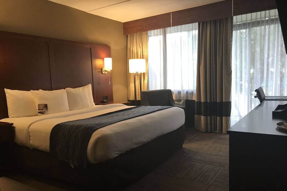 Une chambre d’hôtel avec un grand lit, un bureau, une chaise, une lampe et une vue sur l’extérieur par la fenêtre.