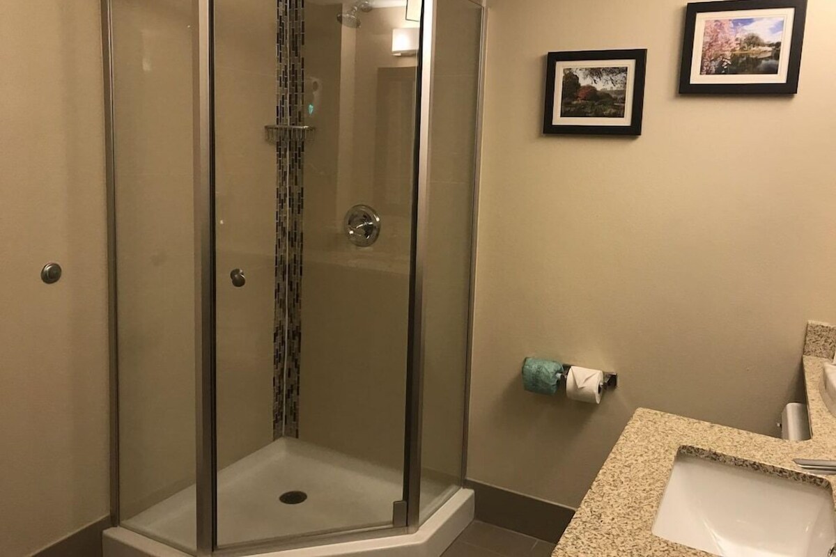 A modern bathroom with a glass-enclosed shower, a toilet paper holder, and framed pictures on the wall.