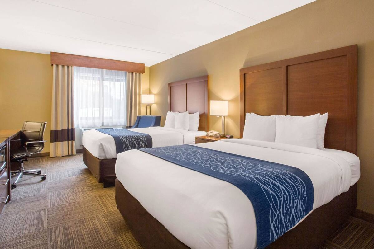 Une chambre d’hôtel avec deux lits, un bureau, une chaise et une lampe.