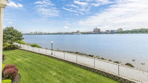 A waterfront view with a stone pathway, a lamp post, and a distant city skyline.