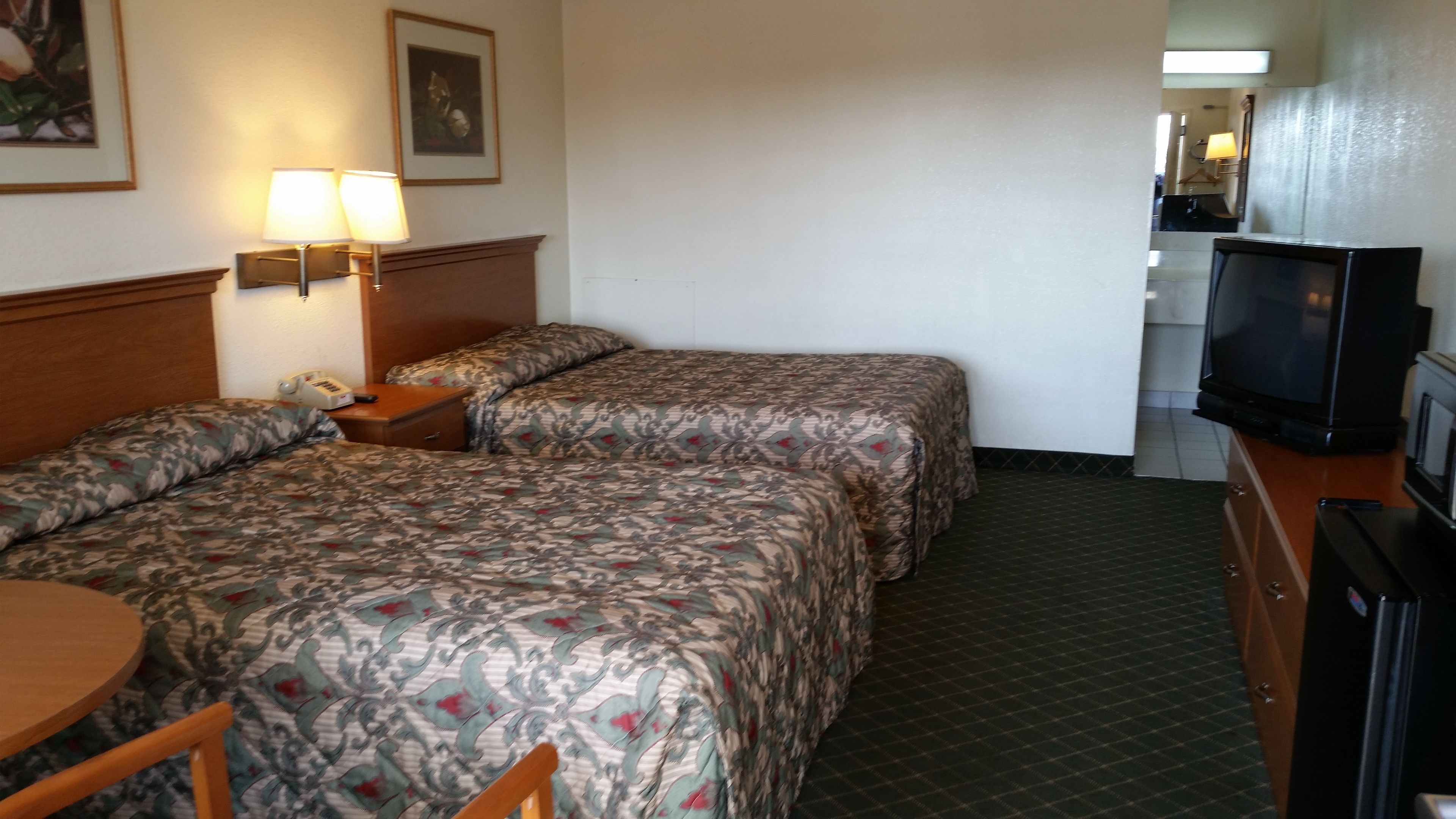 A hotel room with two beds, a desk with a lamp, a telephone, and a television.