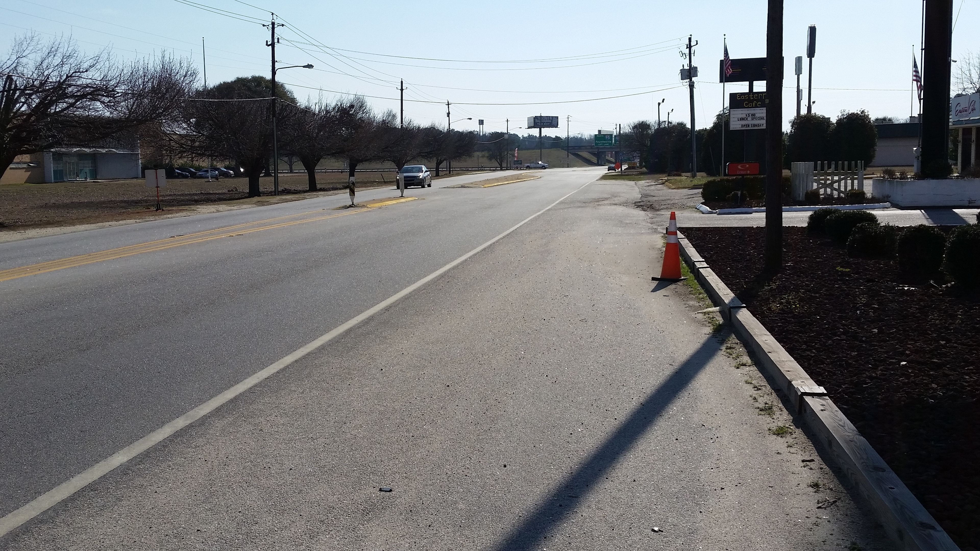 Une route avec un trottoir, un cône de signalisation et un panneau indiquant l’emplacement du café Eastern.
