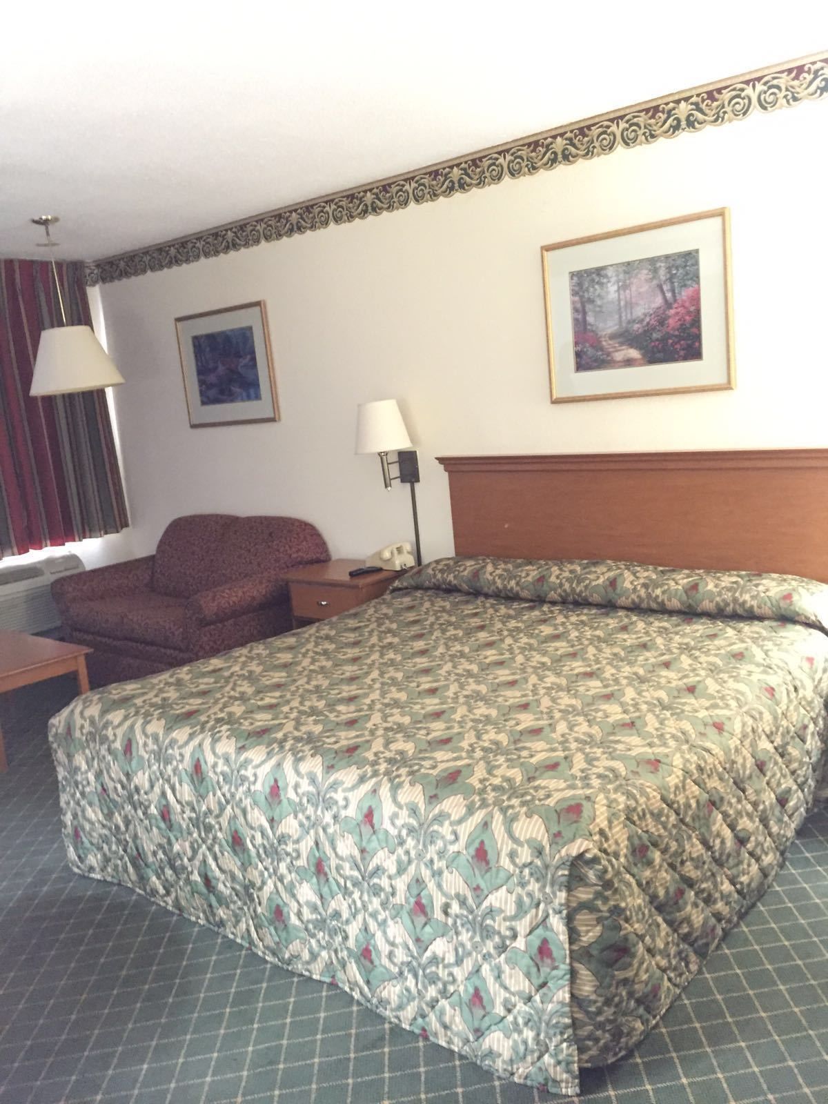 A hotel room with a large bed, a chair, a desk, and two lamps.