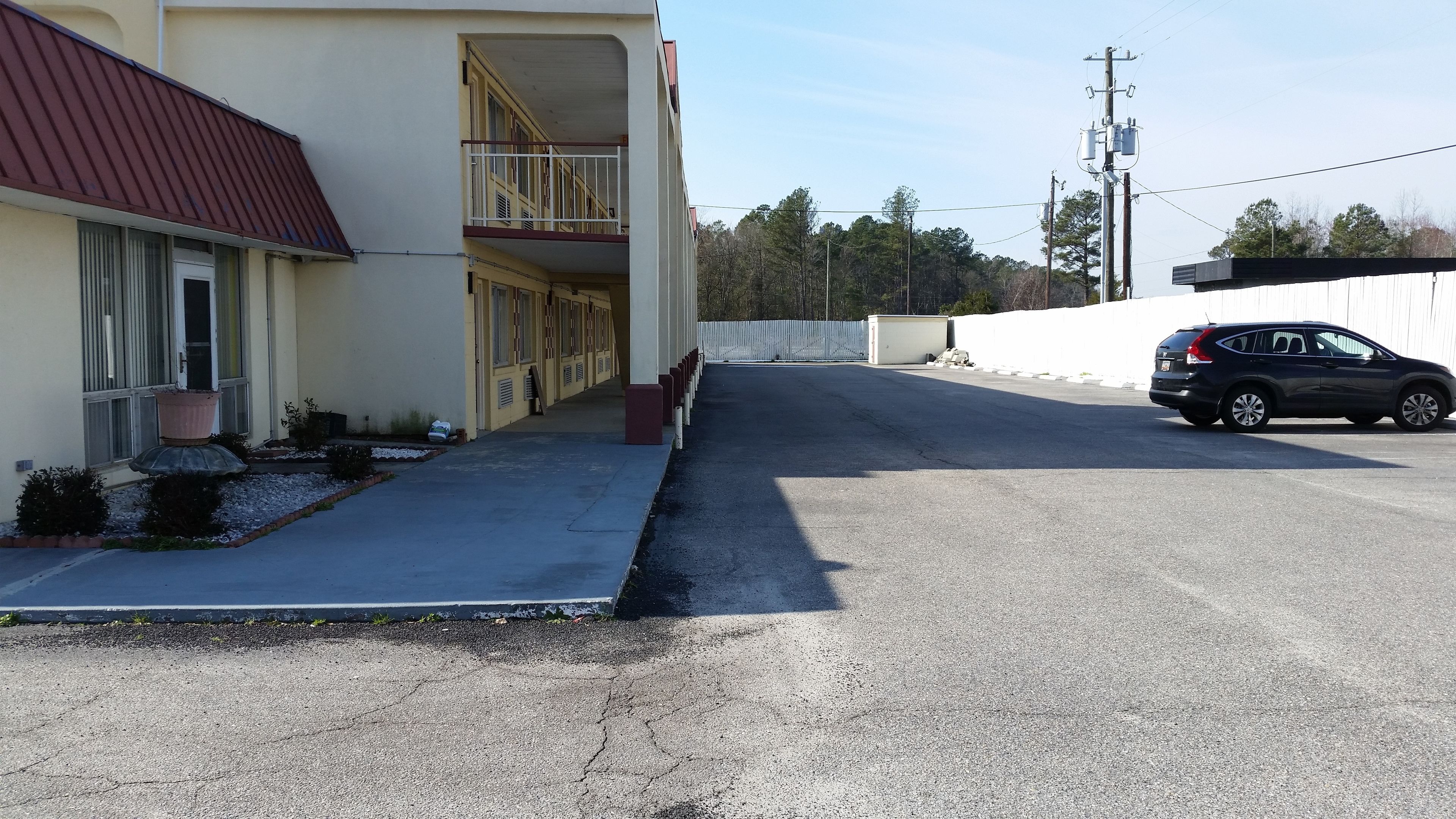 A building with a red roof, a balcony, and a parking area with a black SUV.