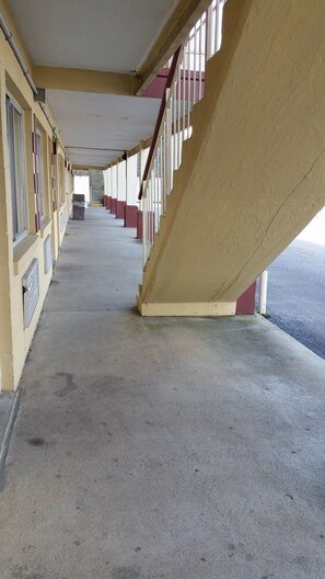 A corridor with a concrete floor, yellow walls, and a red railing. - Economy Inn (Dillon)