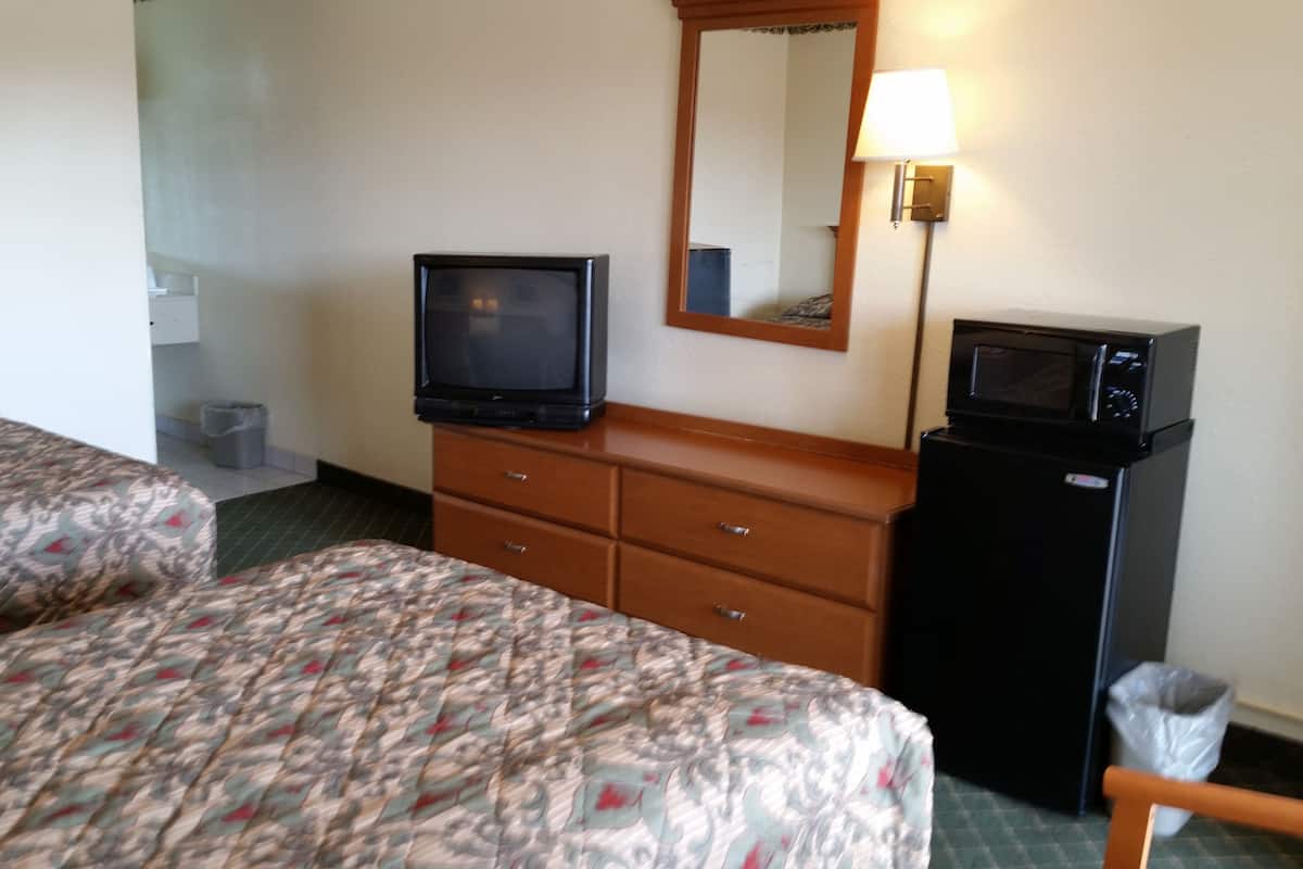 A hotel room with two beds, a television, a microwave, a dresser, and a mirror.