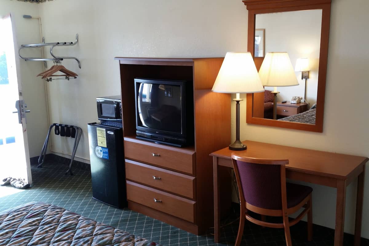A hotel room with a television, a desk with a chair, a lamp, a mirror, and a coat rack with hangers.